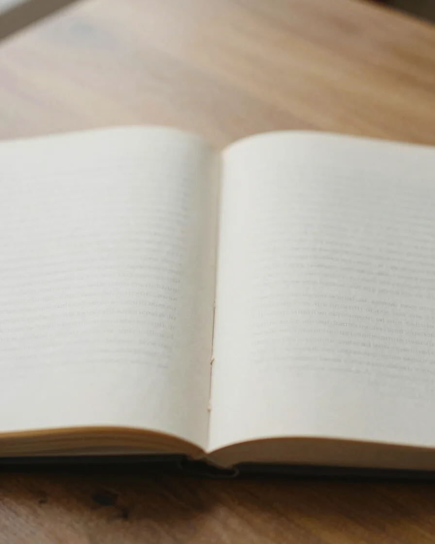 Calm editorial photography of an open book on a wooden table, soft diffused natural daylight, muted earth tones, warm pa
